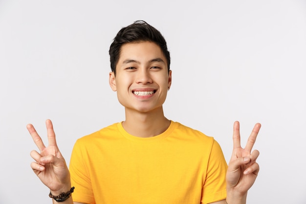 Bonito homem asiático em camiseta amarela, mostrando sinais de vitória