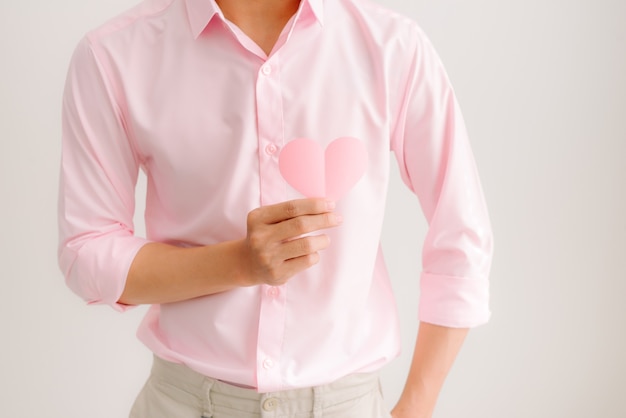 Bonito homem asiático segurando papel de coração rosa posando em fundo cinza