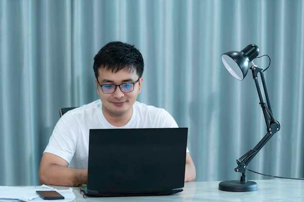 Bonito homem asiático trabalhando em casaTrabalho em casa conceito Trabalhos que você pode fazer em qualquer lugar do mundoUse um computador para trabalhar com um método de controle remoto