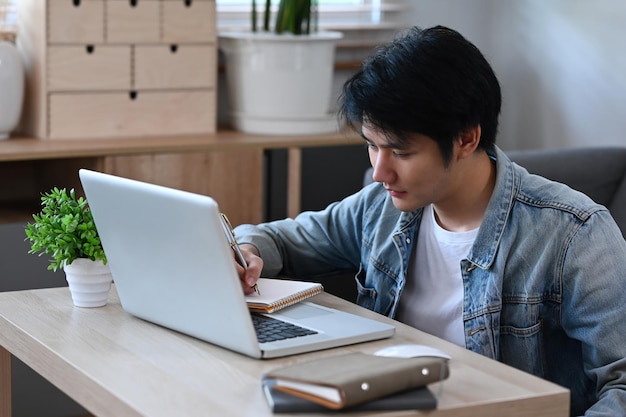 Bonito homem asiático trabalhando estudo on-line no computador portátil em casa