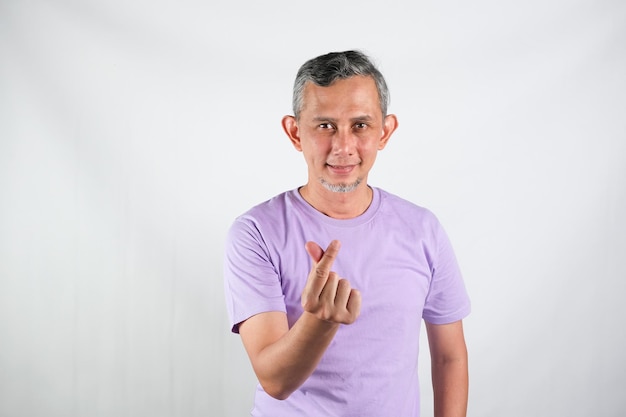 Bonito homem asiático vestindo camiseta sorrindo com coração de sinal de amor com os dedos