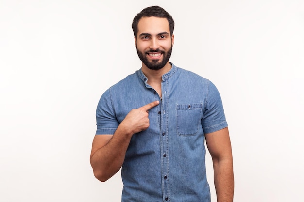 Bonito homem barbudo apontando o dedo sobre si mesmo olhando para a câmera com um sorriso, orgulhoso de seu sucesso e realizações. Tiro de estúdio interior isolado no fundo branco