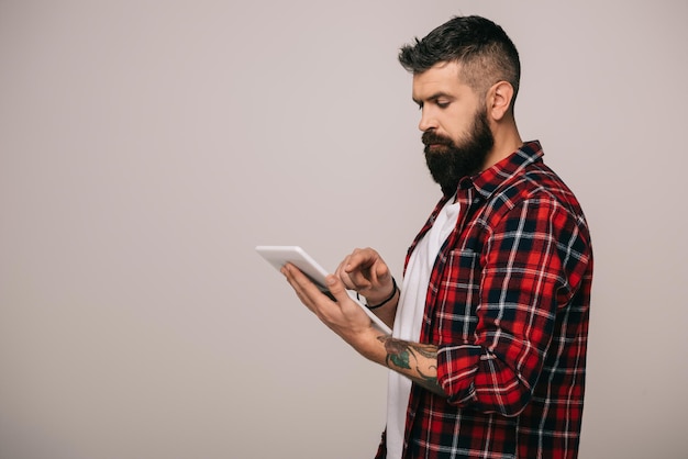 Foto bonito homem barbudo em camisa quadriculada usando tablet digital isolado em cinza