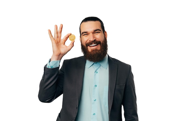 Bonito homem barbudo está segurando um bitcoin dourado enquanto sorri para a câmera
