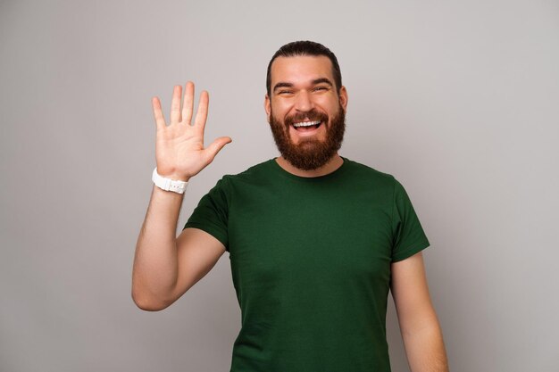 Bonito homem barbudo vestindo camiseta verde está dizendo oi para a câmera