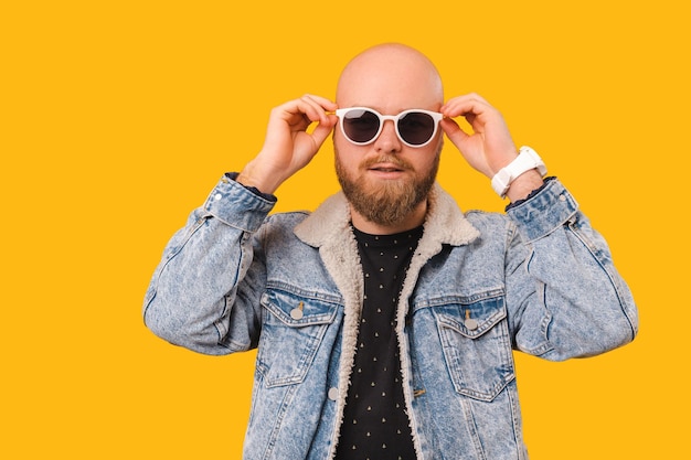 Bonito homem careca barbudo vestindo jeans está segurando óculos de sol brancos legais