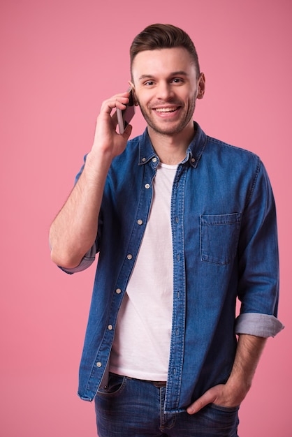 Bonito homem casual moderno está falando no telefone inteligente isolado no fundo rosa