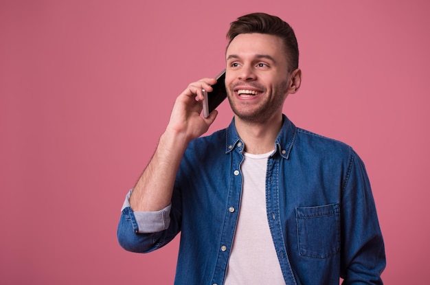 Bonito homem casual moderno está falando no telefone inteligente isolado no fundo rosa