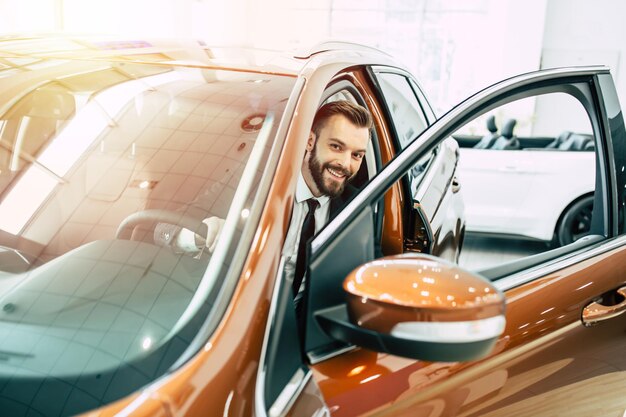 Bonito homem de negócios sorridente de terno completo comprando carro novo na concessionária O vendedor mostra o carro