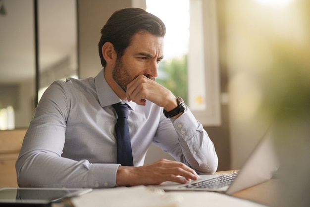 Bonito homem de negócios trabalhando duro no laptop no escritório moderno