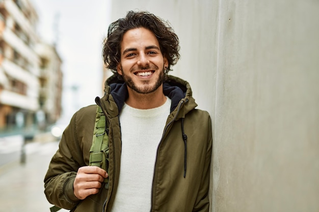 Bonito homem hispânico sorrindo encostado na parede