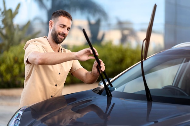 Foto bonito homem latino substituir limpadores de pára-brisa no carro parado ao ar livre. conceito de serviço de carro