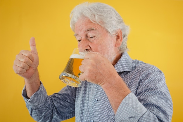 Bonito homem sênior apreciando um copo de cerveja loira fresca polegar para cima fundo amarelo