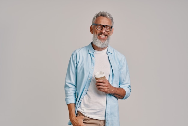 Foto bonito homem sênior olhando para a câmera e sorrindo em pé contra um fundo cinza