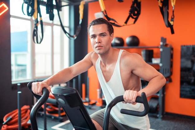 Bonito homem sério sentado na máquina de esportes