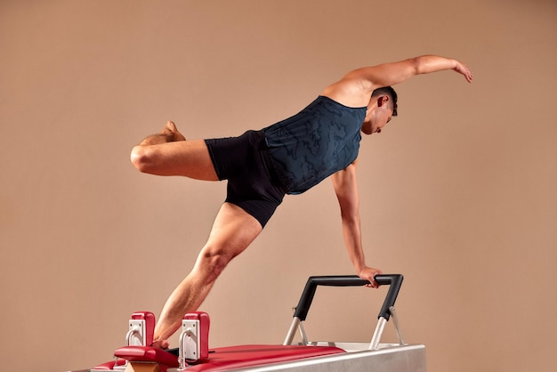 Bonito instrutor masculino de pilates realizando exercício de equilíbrio de alongamento em equipamentos de barril pequeno no interior moderno do estúdio de pilates