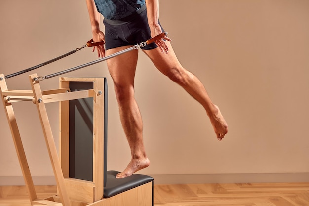 Bonito instrutor masculino de pilates realizando exercício de equilíbrio de alongamento em equipamentos de barril pequeno no interior moderno do estúdio de pilates