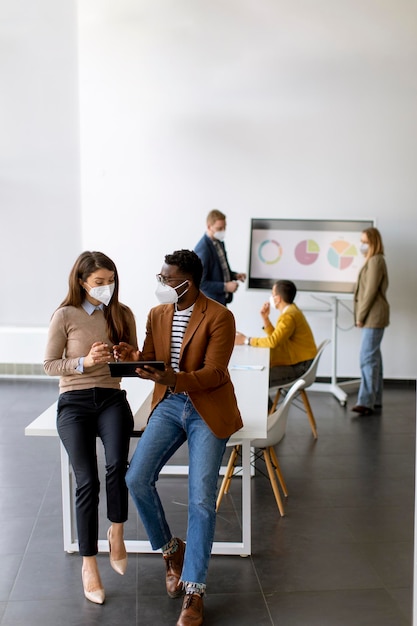 Bonito jovem empresário afro-americano e mulher de negócios bonitinha trabalhando em tablet digital enquanto usava máscaras de proteção facial