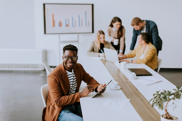 Bonito jovem empresário afro-americano trabalhando com tablet digital na frente de seus colegas de trabalho na sala de reuniões