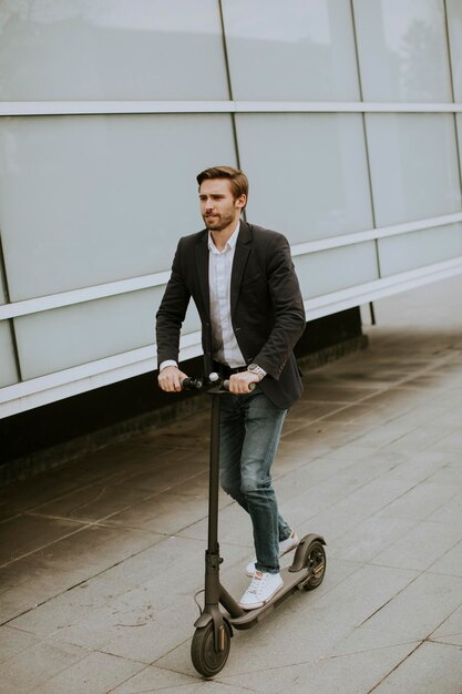 Bonito jovem empresário andando de scooter elétrico na rua pelo prédio de escritórios