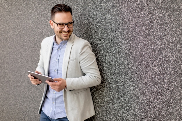 Bonito jovem empresário com tablet digital pela parede cinza