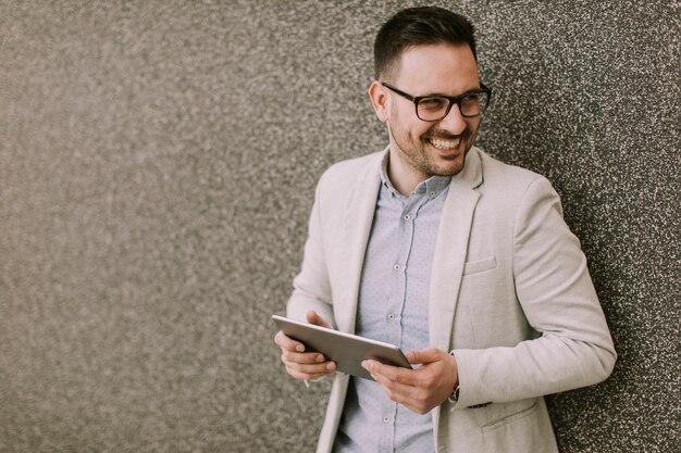 Bonito jovem empresário com tablet digital pela parede cinza