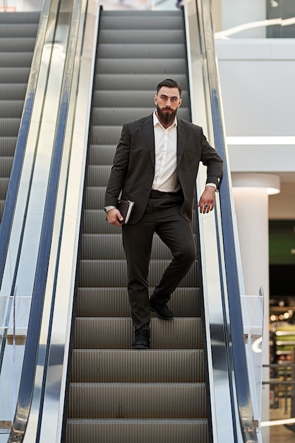 bonito jovem empresário de pé na escada rolante. Conceito de negócios.