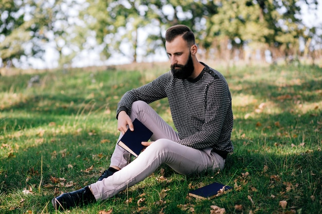 Bonito jovem estudante barbudo homem hipster lendo livro no parque no dia ensolarado de verão