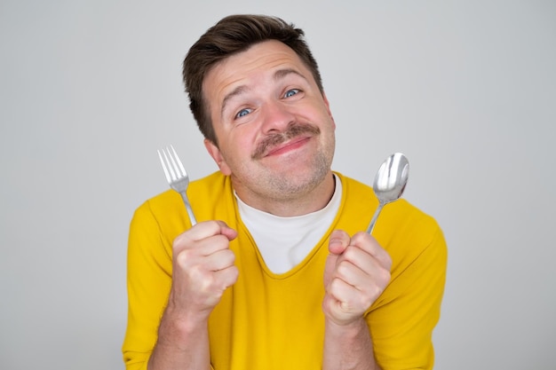 Bonito jovem faminto segurando garfo e colher esperando o jantar