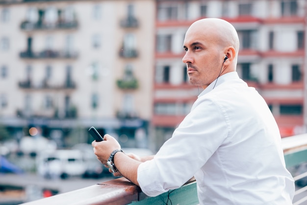 Bonito, jovem, homem negócios, em, um, camisa branca, inclinado, ligado, handrail, e, escutar música