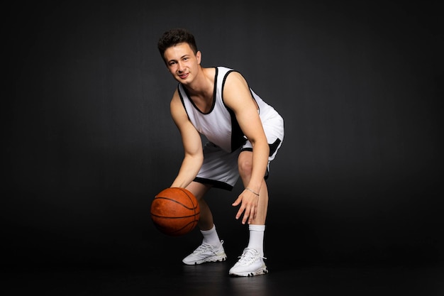 Bonito jovem jogador de basquete em roupas esportivas brancas isoladas em fundo preto