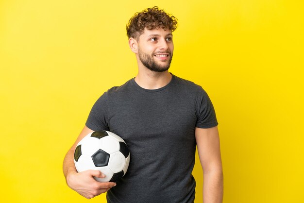 Bonito jovem jogador de futebol isolado em fundo amarelo pensando em uma ideia enquanto olha para cima