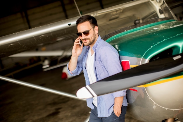 Bonito, jovem, piloto, verificar, avião, em, hangar, e, usando, telefone móvel