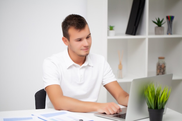 Bonito jovem trabalhador trabalhando em um escritório da empresa com documentos e um laptop