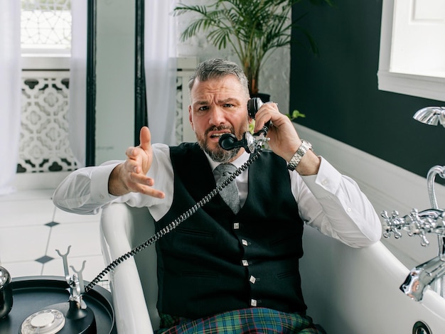 bonito maduro corajoso homem elegante escocês de kilt e terno falando ao telefone de casa