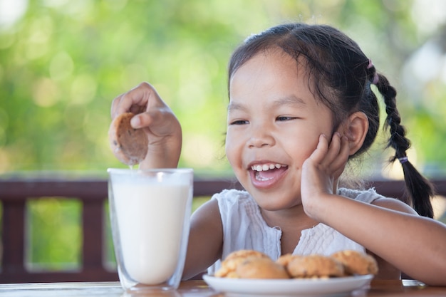 Bonito menina asiática criança comendo biscoito com leite no café da manhã