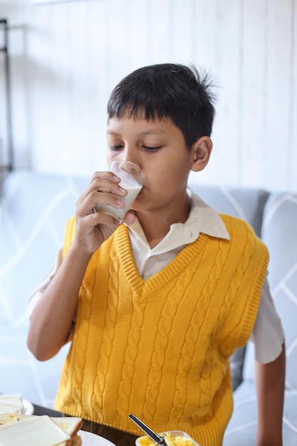 Bonito menino asiático bebe leite, tomando café da manhã antes de ir para a escola.