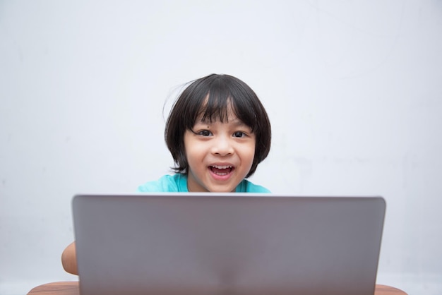 Bonito menino asiático inteligente está felizmente usando seu laptop para estudar online sozinho em casa Conceito de aprendizado onlineAutoestudo