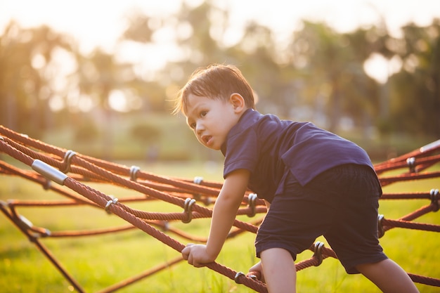 Bonito menino criança asiática se divertindo para brincar e subir na corda no playground