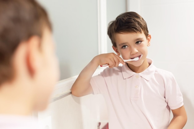 Bonito menino de olhos verdes escovando os dentes na frente de um espelho