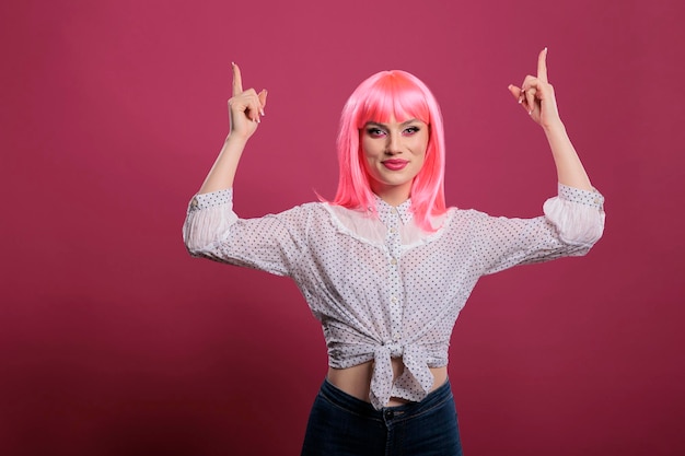 Bonito modelo alegre apuntando hacia arriba con los dedos índices en el estudio, posando con los brazos levantados para indicar el anuncio hacia arriba. Indicando y recomendando direcciones con las manos frente a la cámara.