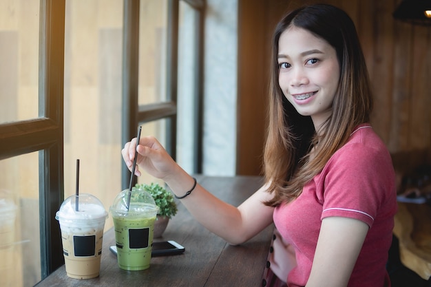 Bonito, mulher asian, em, loja café, olhando câmera, com, cappuccino gelado, e, matcha, chá verde