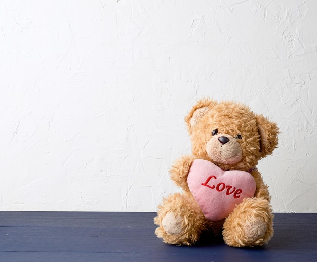 bonito oso de peluche marrón sosteniendo un gran corazón rosa y se sienta en un regalo de vacaciones de fondo de madera para