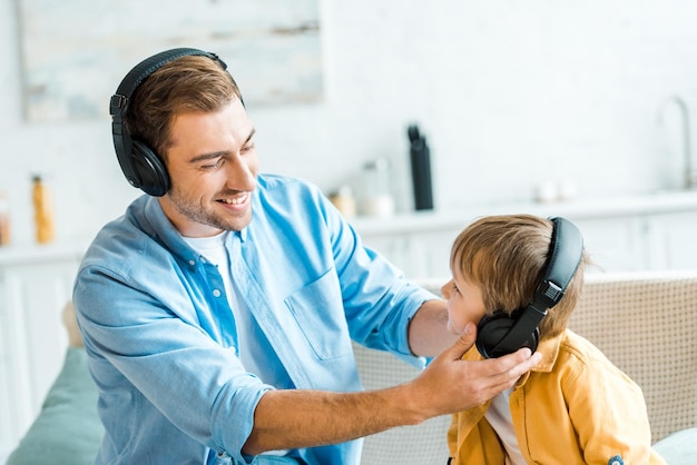 Bonito pai sorridente com filho pré-escolar em fones de ouvido ouvindo música em casa