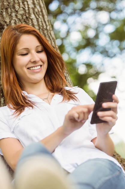 Foto bonito pelirrojo mensajes de texto en su teléfono en el parque en un día soleado