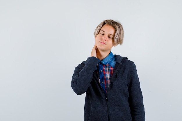 Bonito rapaz adolescente com camisa, capuz, sentindo dor no pescoço e parecendo cansado, vista frontal.