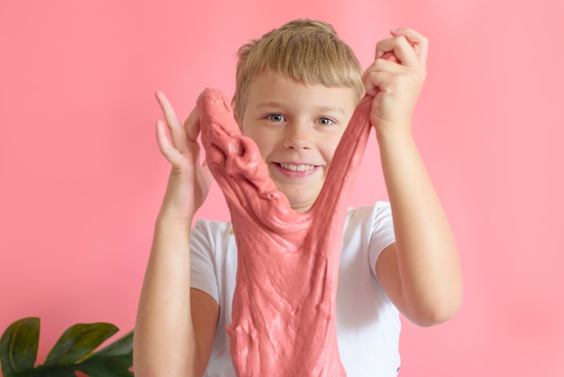 Bonito rapaz loiro brincando com gosma artesanal em fundo rosa