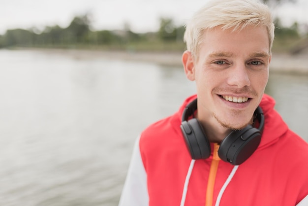 Bonito sorridente atraente loiro homem bonito com fones de ouvido no pescoço andando e relaxando no parque da cidade Estilo de moda de rua Pessoas estilo de vida e conceito de tecnologia