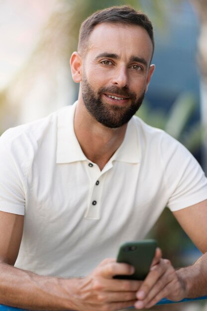 Bonito sorridente homem latino segurando o celular olhando para a câmera na rua da cidade. Banco móvel