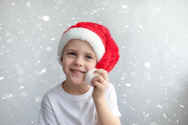 Bonito sorridente menino feliz em um boné vermelho de Natal. Fundo de neve leve. Conceito de Natal, atmosfera de ano novo.